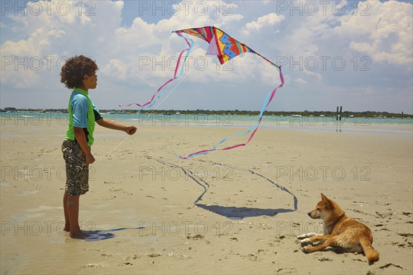 Mixed race boy flying kite on beach