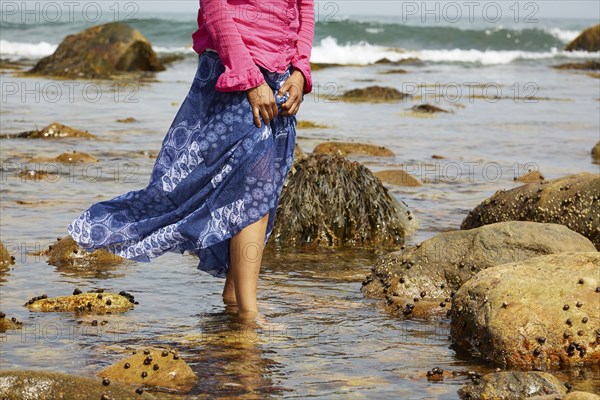 Mixed race woman walking in water on rocky beach