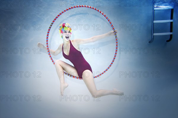 Smiling Caucasian woman holding plastic hoop and wearing vintage bathing suit and cap underwater