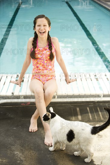 Hispanic girl with cat laughing on lounge chair at swimming pool