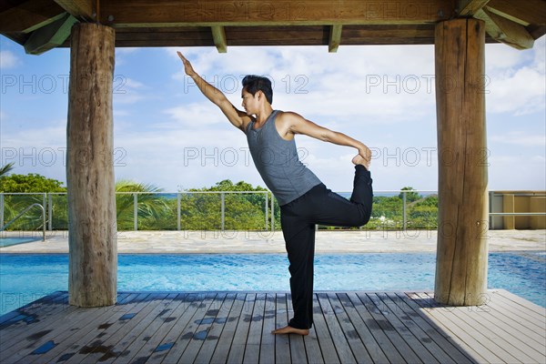 Asian man practicing yoga at poolside