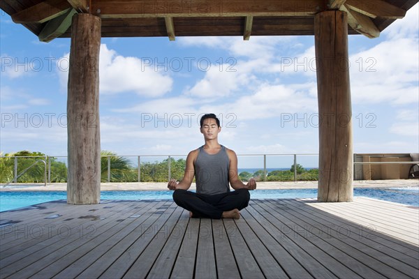 Asian man practicing yoga at poolside