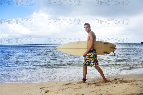 Caucasian man walking on beach carrying surfboard