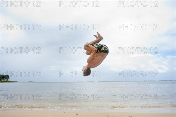 Caucasian man doing a flip on beach
