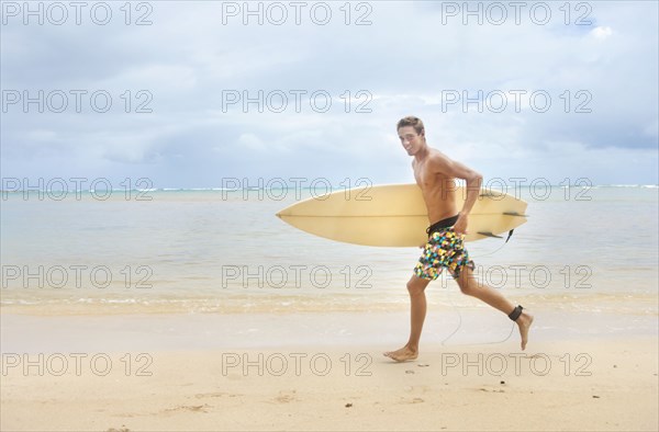 Caucasian man running on beach carrying surfboard