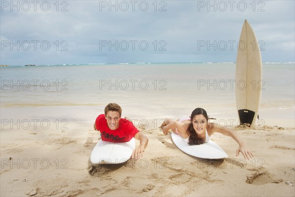 Couple laying on surfboards on beach