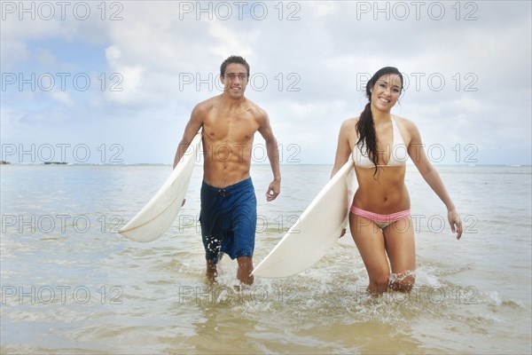 Couple walking in ocean carrying surfboards
