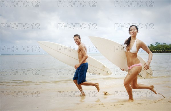 Couple running on beach carrying surfboards