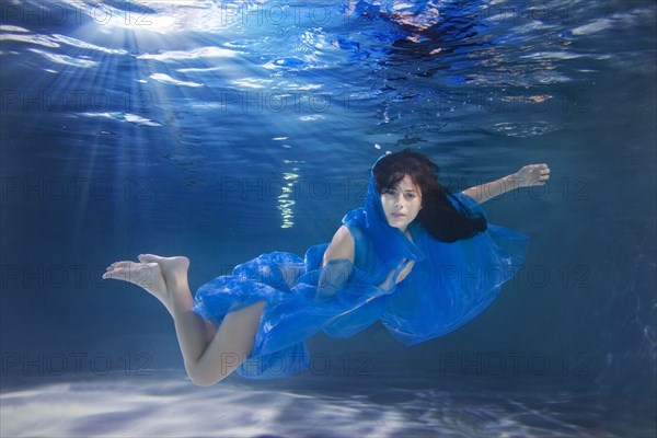 Hispanic woman swimming underwater with scarf