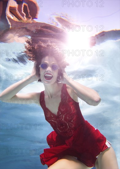 Mixed race woman in clothes swimming underwater