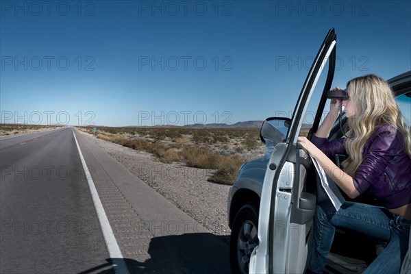 Caucasian woman parked on roadside using binoculars