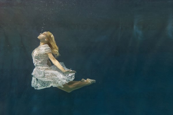 Caucasian woman in dress swimming under water