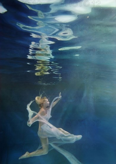 Caucasian woman in dress swimming under water