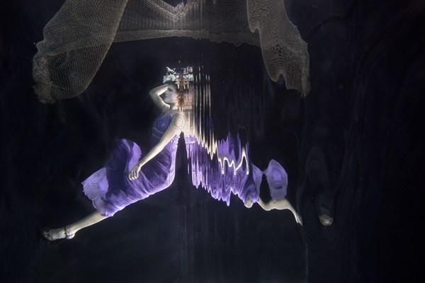 Caucasian woman in dress swimming under water