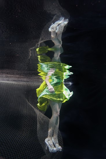 Caucasian woman in dress swimming under water