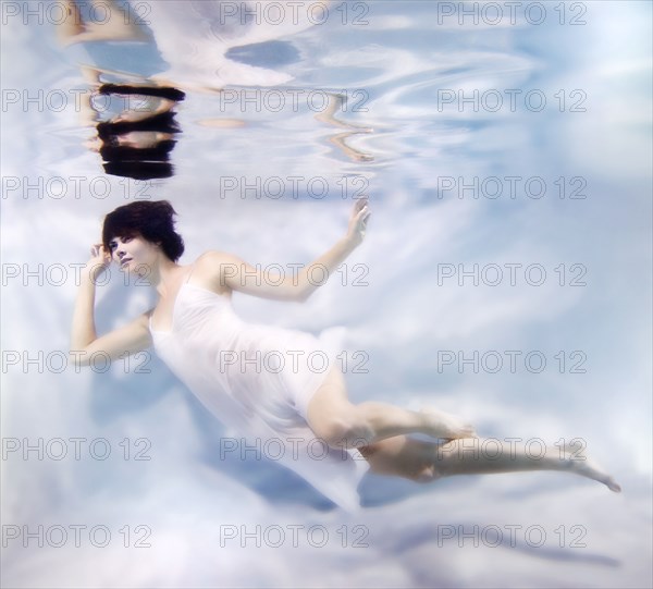 Caucasian woman in dress swimming under water