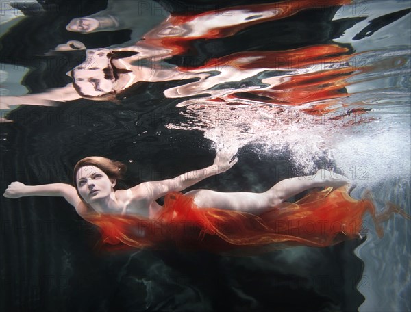 Caucasian woman in dress swimming under water