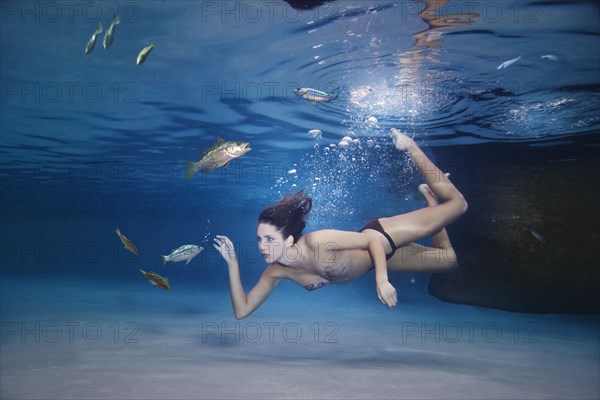 Mixed race woman swimming in water with fish