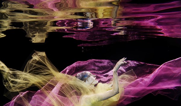 Caucasian woman in scarf swimming under water