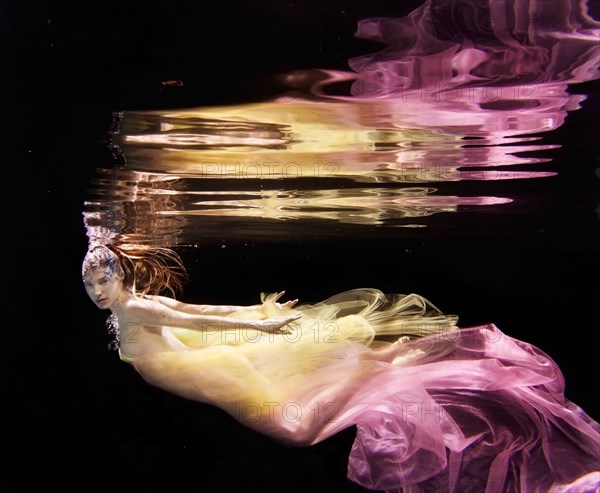 Caucasian woman in dress swimming under water