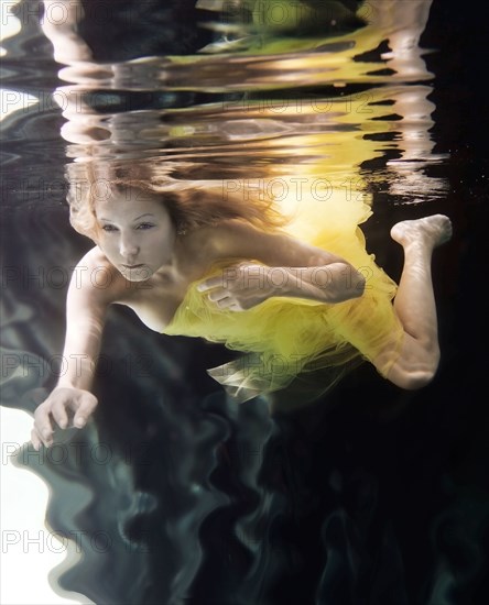 Caucasian woman in dress swimming under water