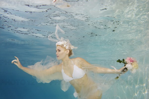 Caucasian bride in bikini swimming under water