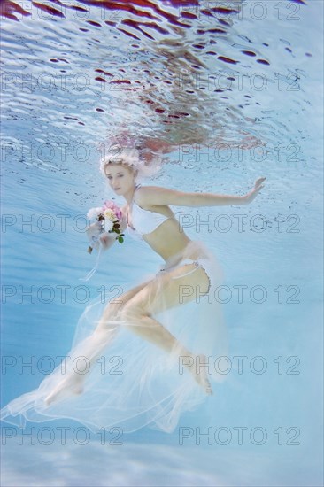 Caucasian bride in bikini swimming under water