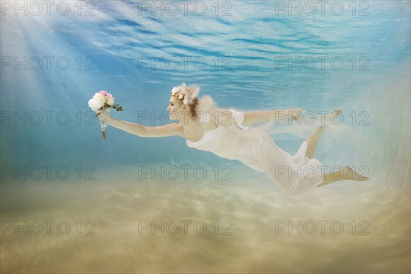 Caucasian bride in wedding dress swimming under water