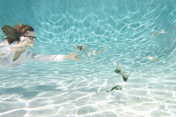 Caucasian businesswoman reaching for money underwater