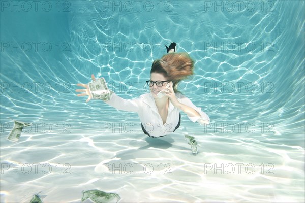 Caucasian businesswoman reaching for money underwater
