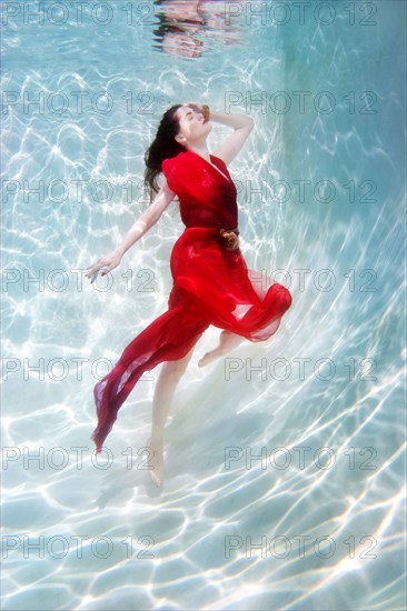 Mixed race woman in dress underwater in swimming pool