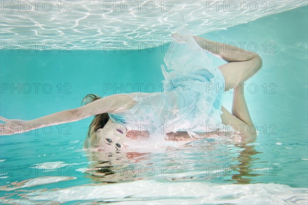 Mixed race woman in dress underwater in swimming pool