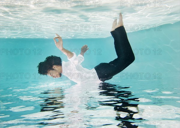 Mixed race man in clothes underwater in swimming pool