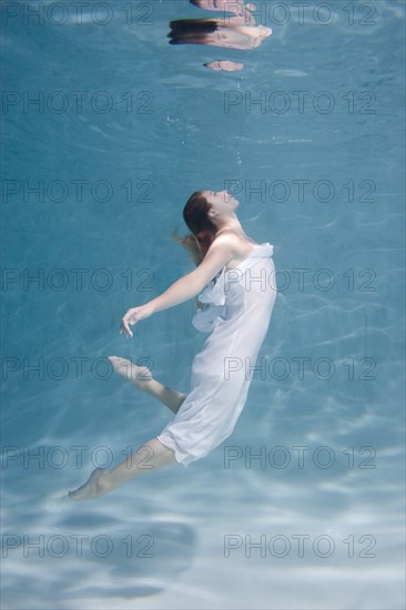 Underwater view of Caucasian woman in dress swimming in pool