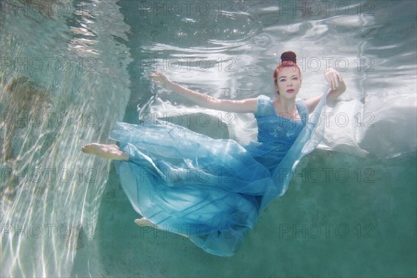 Underwater view of Caucasian woman in dress swimming in pool