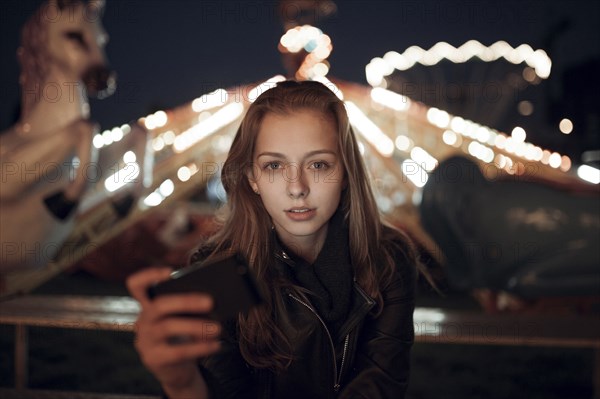 Caucasian teenage girl holding cell phone at amusement park