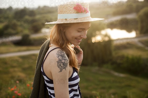 Smiling Caucasian woman wearing sun hat carrying sweater