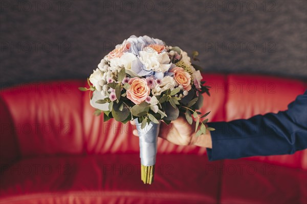 Caucasian man holding bouquet of flowers near red sofa