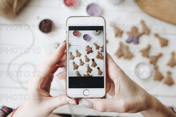 Hands of Caucasian woman photographing Christmas cookies with cell phone