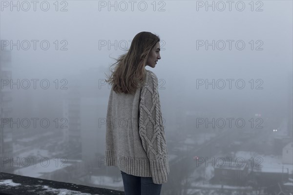 Caucasian woman admiring cityscape on rooftop in winter