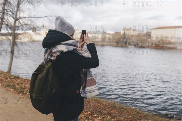 Caucasian woman photographing river with cell phone