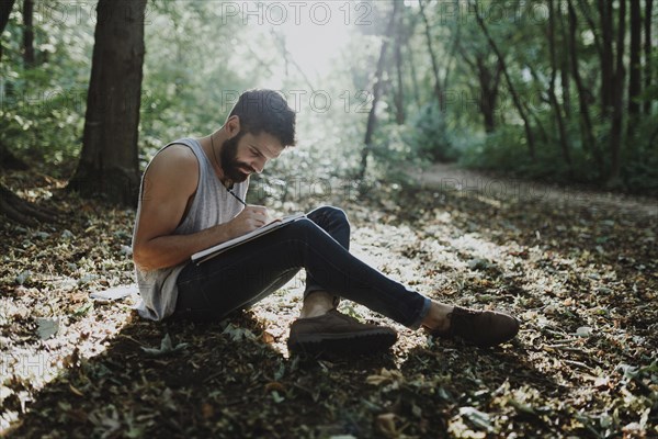 Caucasian man sitting in woods drawing on sketchpad