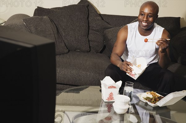 African man on sofa eating take out food