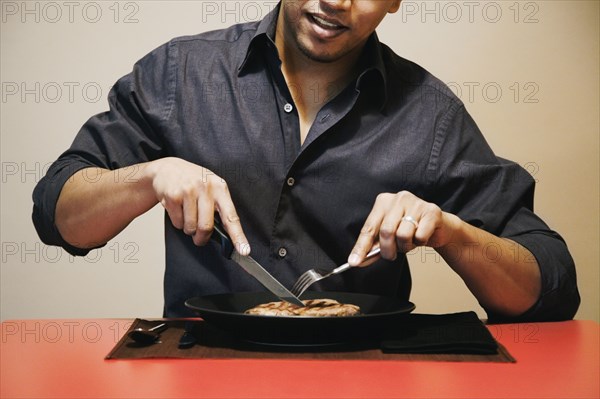 Asian man cutting meat on plate