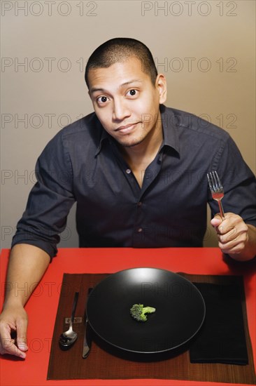 Asian man with one piece of broccoli on plate