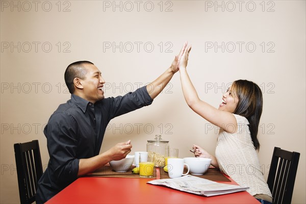 Asian couple high-fiving at breakfast table