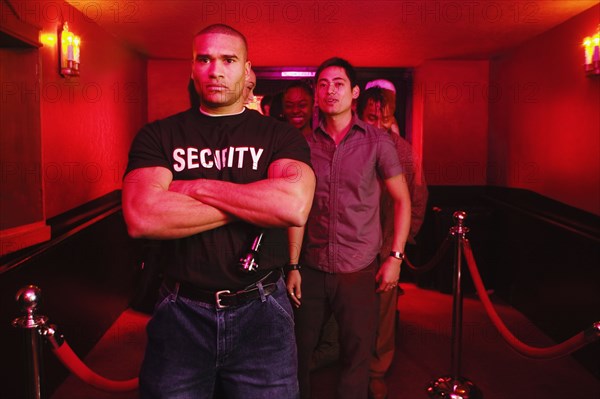 African male bouncer with arms crossed in front of people