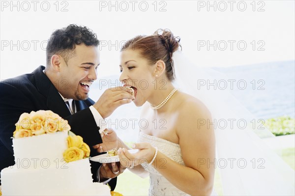 Multi-ethnic bride and groom eating cake