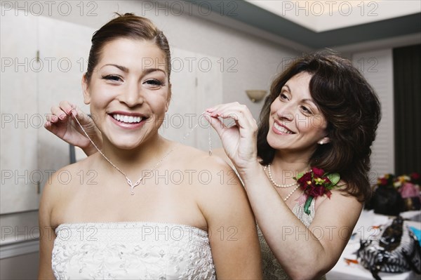 Bride's mother putting necklace on daughter