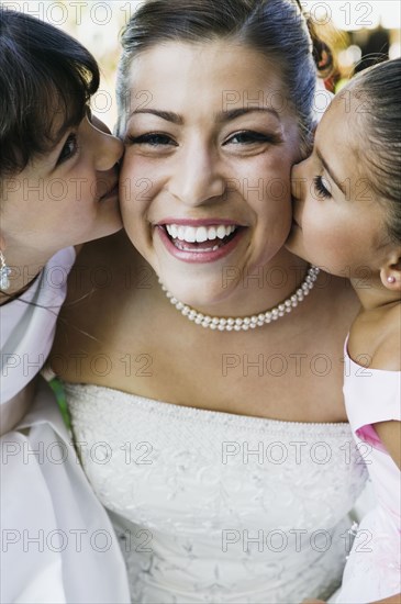 Two girls kissing bride on cheeks